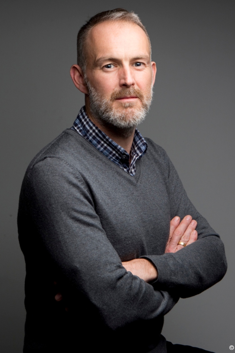 An image of Mark with his arms crossed, wearing a grey jumper, 