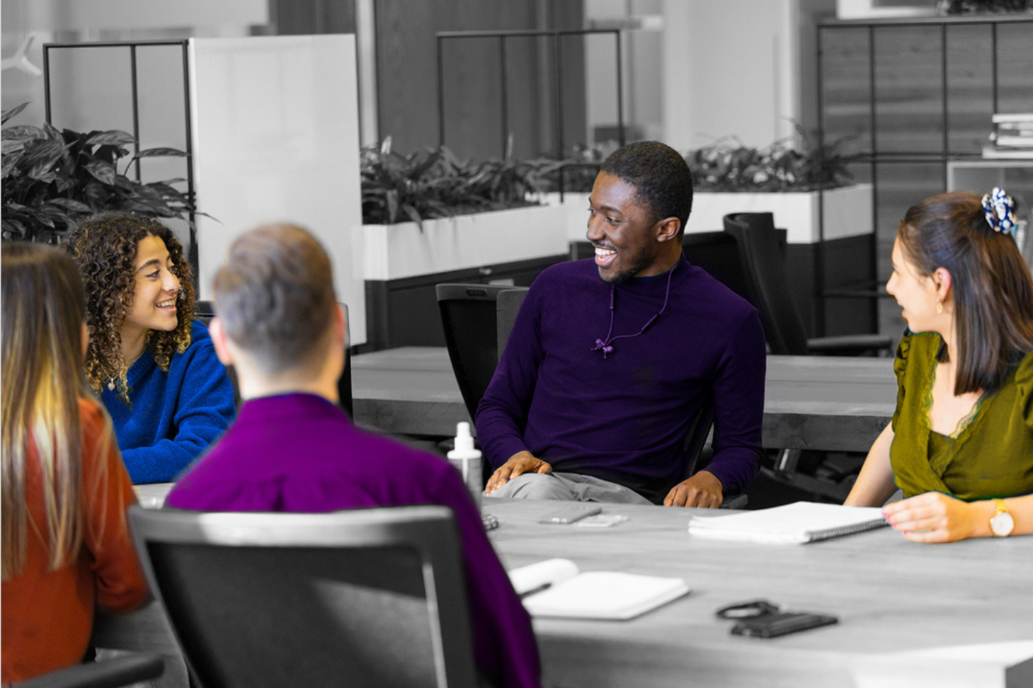 Black and White image, where only clothes and skin tone are in colour. This photo shows four young people working in a open meeting together