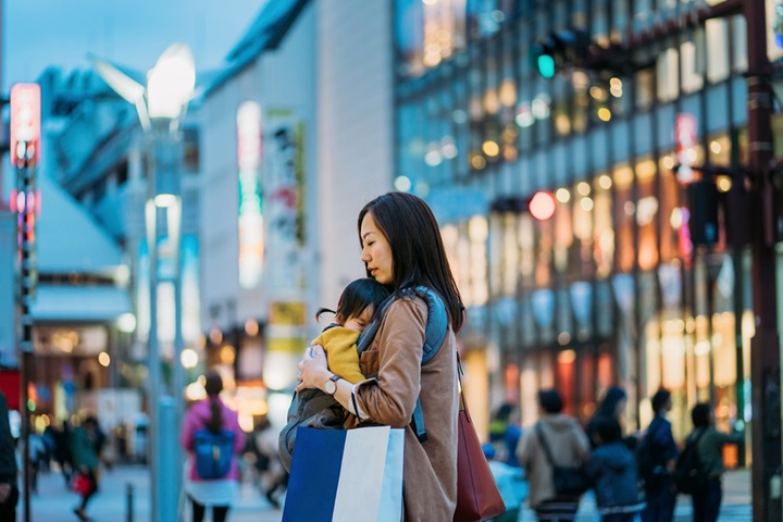 Young Asian mother carrying shopping bag walking in downtown city street