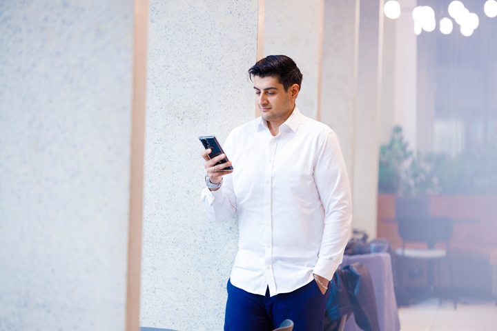 A man looking at his mobile phone while leaning against a pillar. 